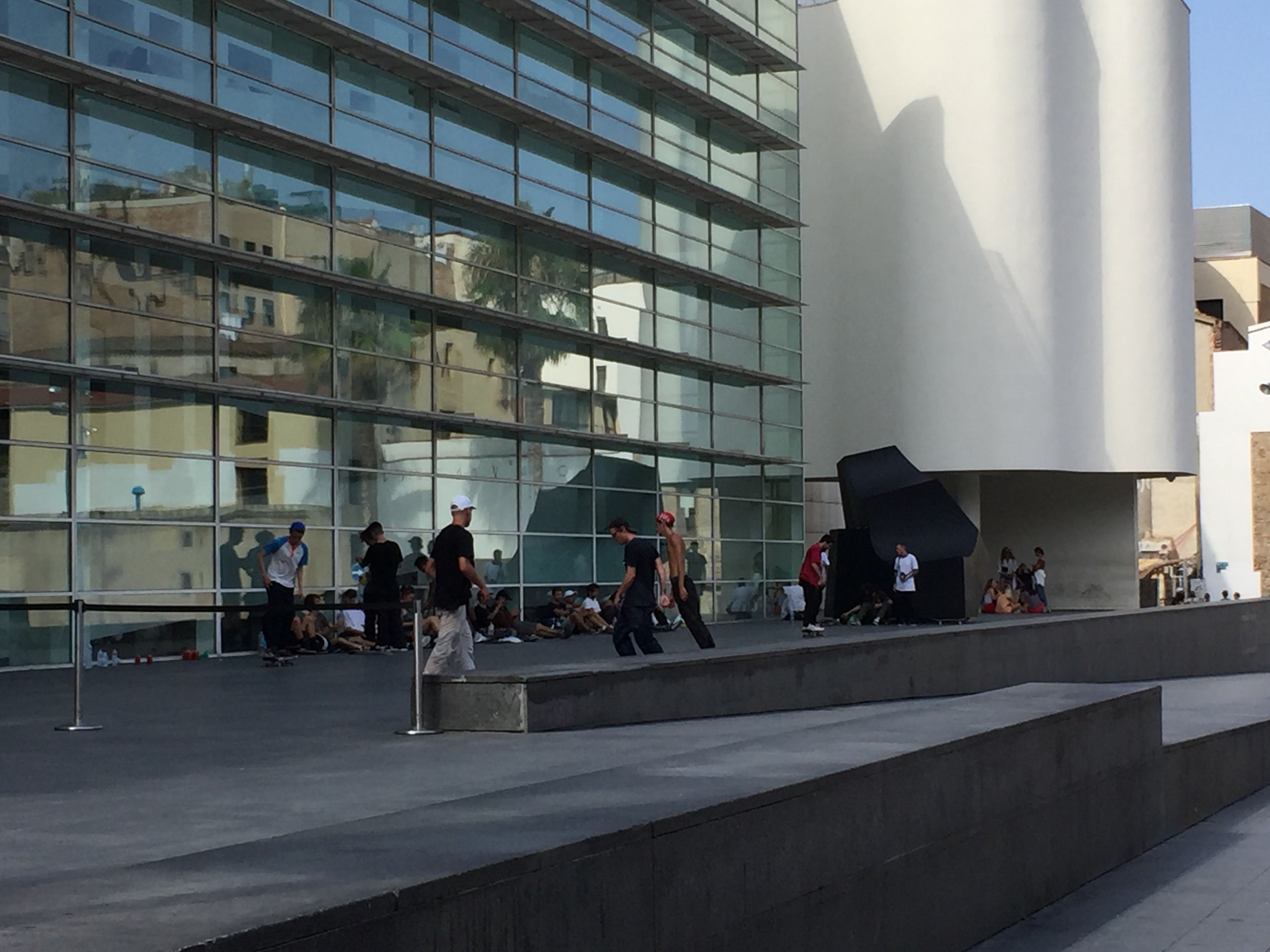 Museu d’Art Contemporani de Barcelona- The  facade of the structure emphasizes an abundance of purposefully angled glass focused in a direction that maximizes natural lighting during the times of day the museum is open.  Inadvertently, the front of the building also features numerous daredevil skateboarders.