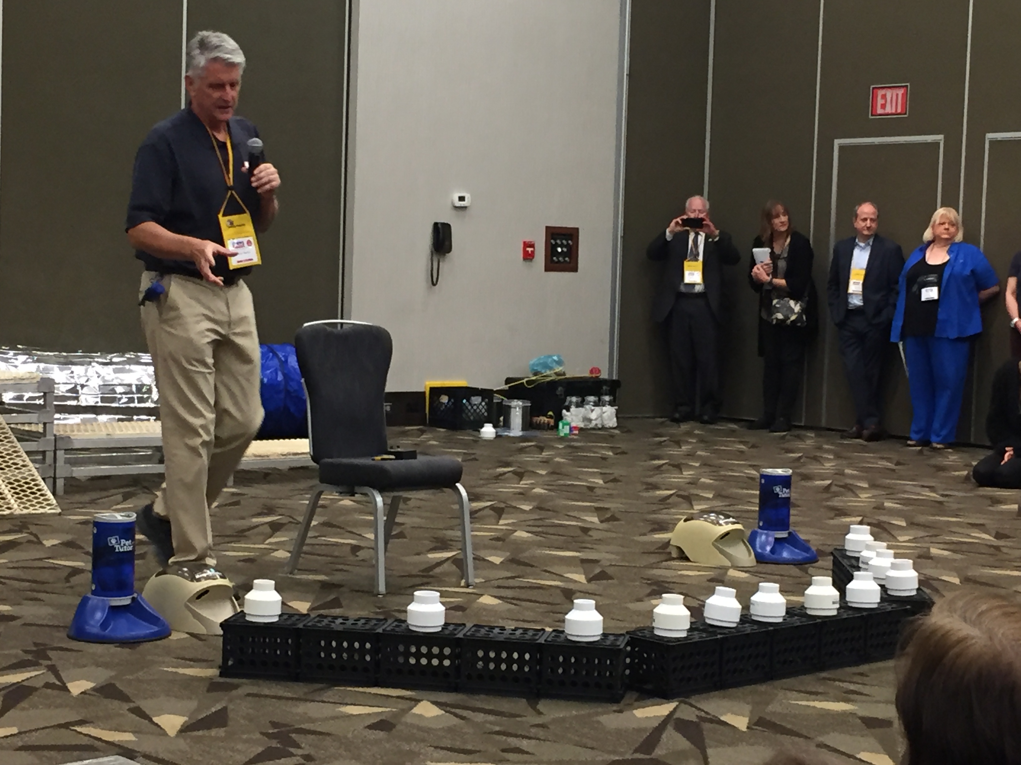 2019 AKC US Detection Dog Conference.  Scott describing the setup he uses to imprint young scent detection dogs.  The setup includes PVC pipes that contain blanks, interferents, or the target odor and 2 Pet Tutor remote feeders, so that the dog learns to focus principally on task, rather than social cues.